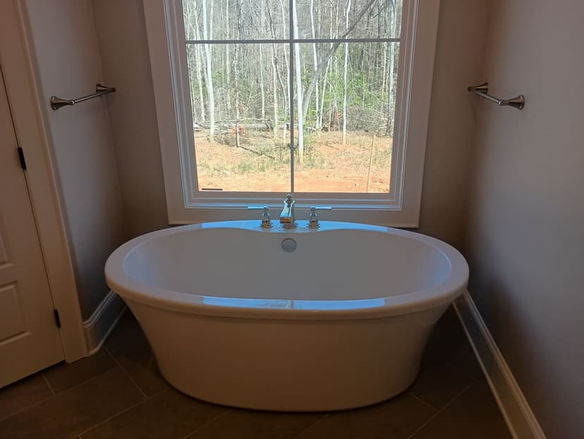 Modern freestanding bathtub by a large window overlooking a serene wooded view.